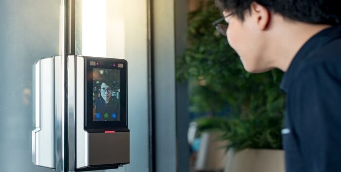 Authentication by facial recognition concept. Biometric admittance control device for security system. Asian man using face scanner to unlock glass door in office building.